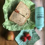 sandwich in wax paper, 3 strawberries in wax paper, an apple and a reusable water bottle