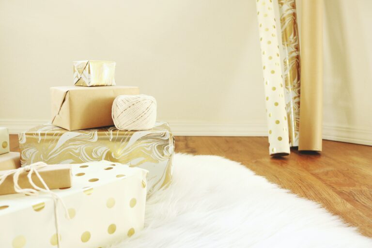 Gift wrapped presents in gold and white with wrapping paper in the background.