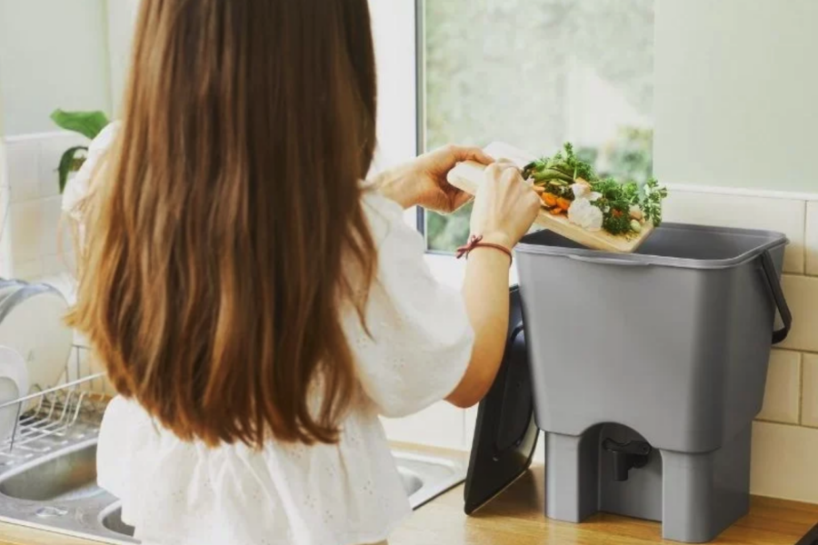 A woman using a small grey food bin to recycle her food waste.