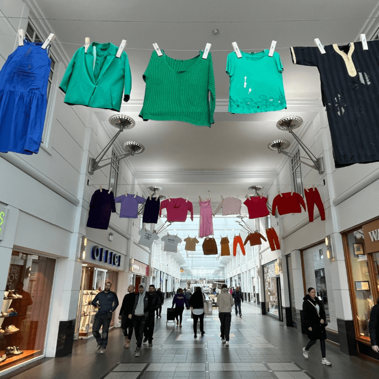 large washing line full of damaged clothing hanging over the walkway in a shopping centre.